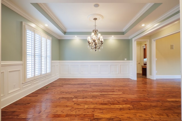 unfurnished room with a tray ceiling, crown molding, wood-type flooring, and a notable chandelier