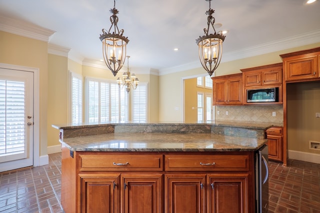 kitchen with stainless steel microwave, dark stone counters, pendant lighting, decorative backsplash, and ornamental molding