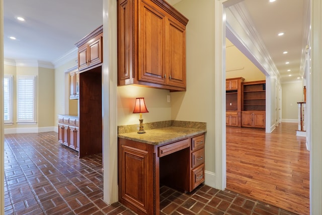 kitchen with light stone countertops, dark hardwood / wood-style flooring, built in desk, and crown molding