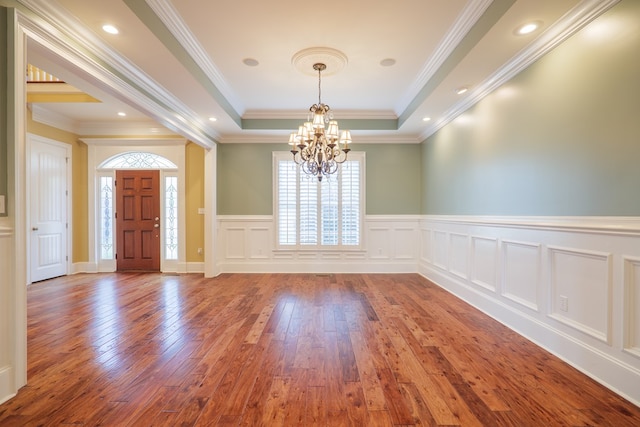 foyer with a tray ceiling, an inviting chandelier, wood-type flooring, and ornamental molding