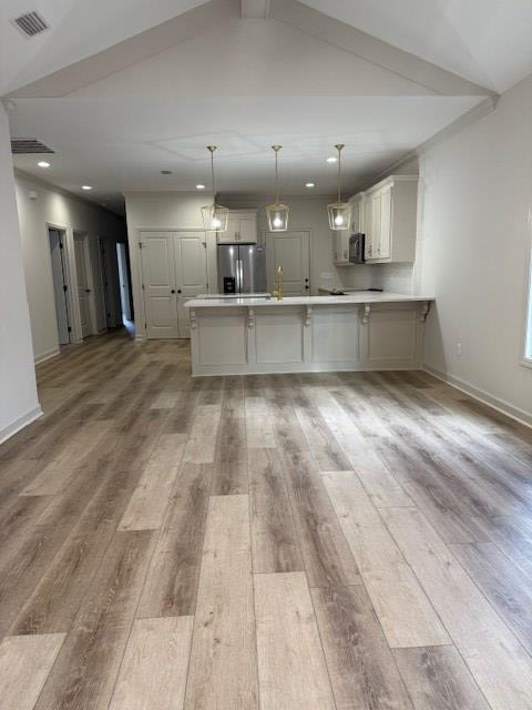 kitchen featuring light hardwood / wood-style flooring, a breakfast bar area, hanging light fixtures, stainless steel fridge with ice dispenser, and kitchen peninsula