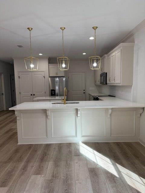 kitchen with sink, stainless steel fridge, white cabinetry, decorative light fixtures, and kitchen peninsula