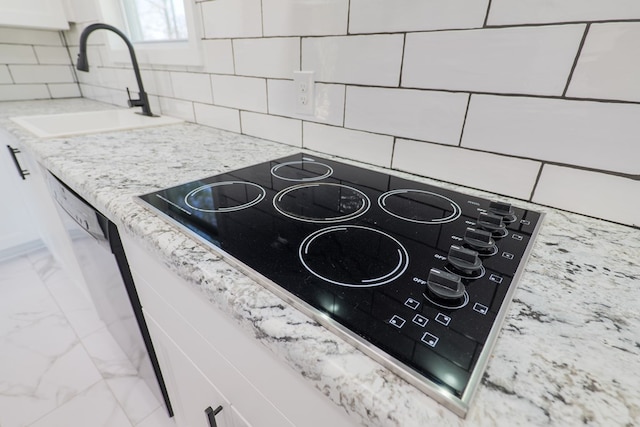 interior details with white cabinets, decorative backsplash, light stone countertops, black electric stovetop, and a sink