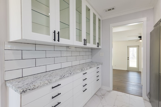 kitchen with marble finish floor, visible vents, decorative backsplash, white cabinets, and baseboards