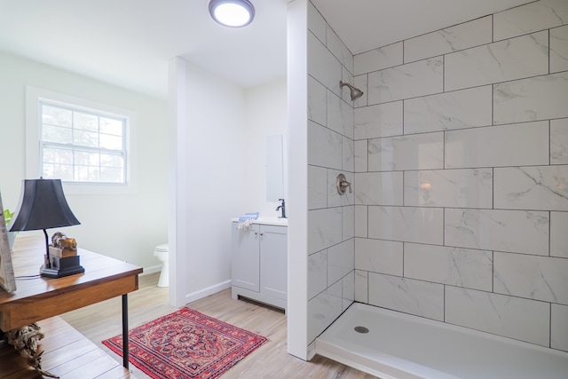 bathroom with hardwood / wood-style flooring, toilet, vanity, and a tile shower