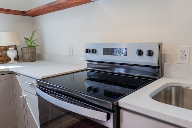 kitchen featuring light stone countertops, electric range, sink, and white cabinetry