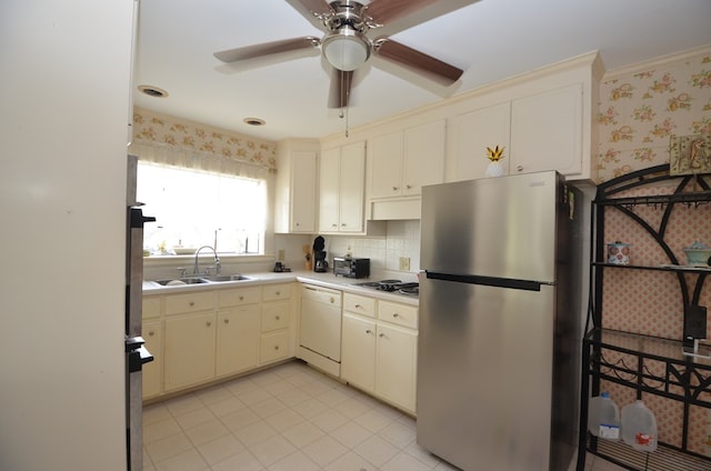 kitchen featuring wallpapered walls, white dishwasher, freestanding refrigerator, a sink, and cream cabinetry