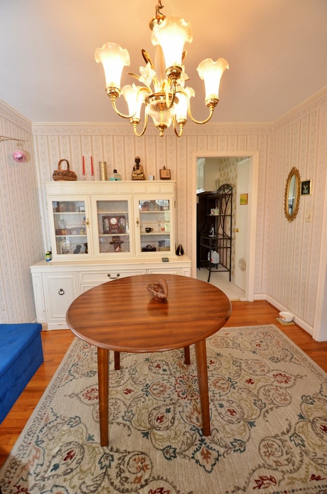 dining space featuring light wood finished floors, an inviting chandelier, crown molding, and wallpapered walls