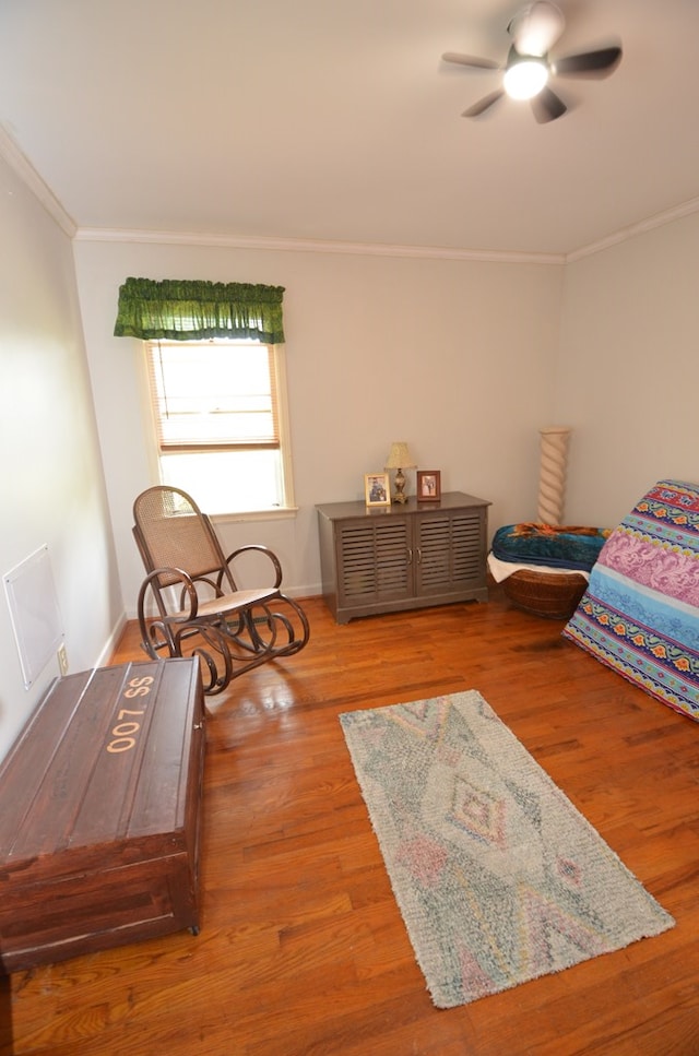 sitting room with baseboards, crown molding, a ceiling fan, and wood finished floors