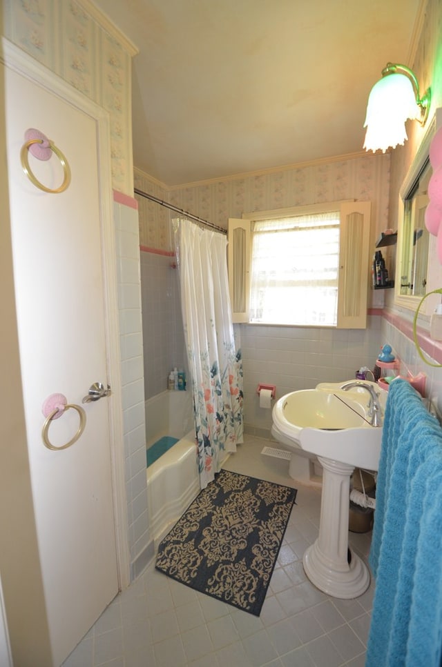 bathroom with tile patterned floors, shower / tub combo with curtain, a sink, tile walls, and wallpapered walls