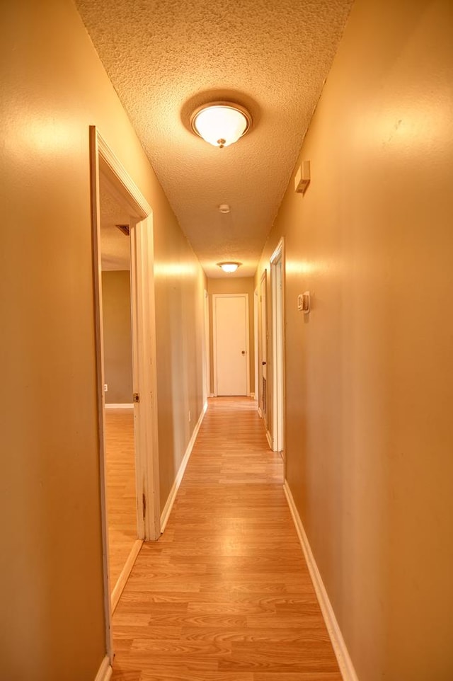 corridor with a textured ceiling and light hardwood / wood-style flooring