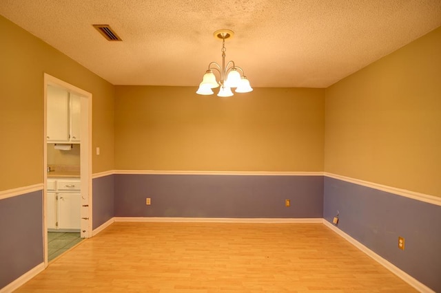 spare room with a textured ceiling, light hardwood / wood-style floors, and a notable chandelier