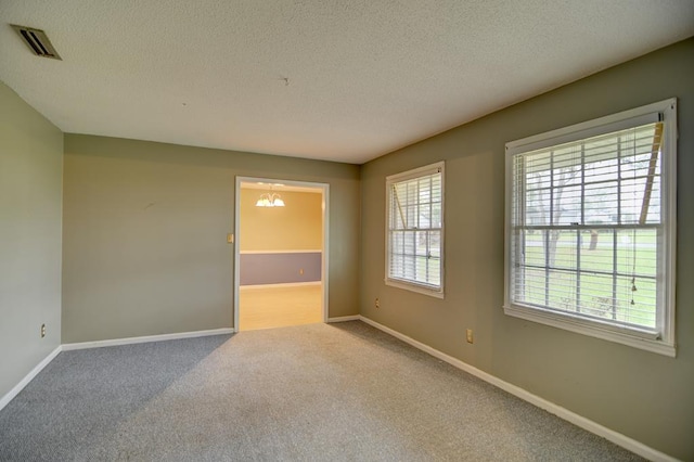 unfurnished room with light colored carpet, a textured ceiling, and an inviting chandelier