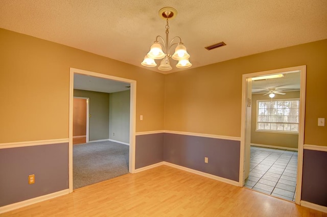 unfurnished room with ceiling fan with notable chandelier, wood-type flooring, and a textured ceiling