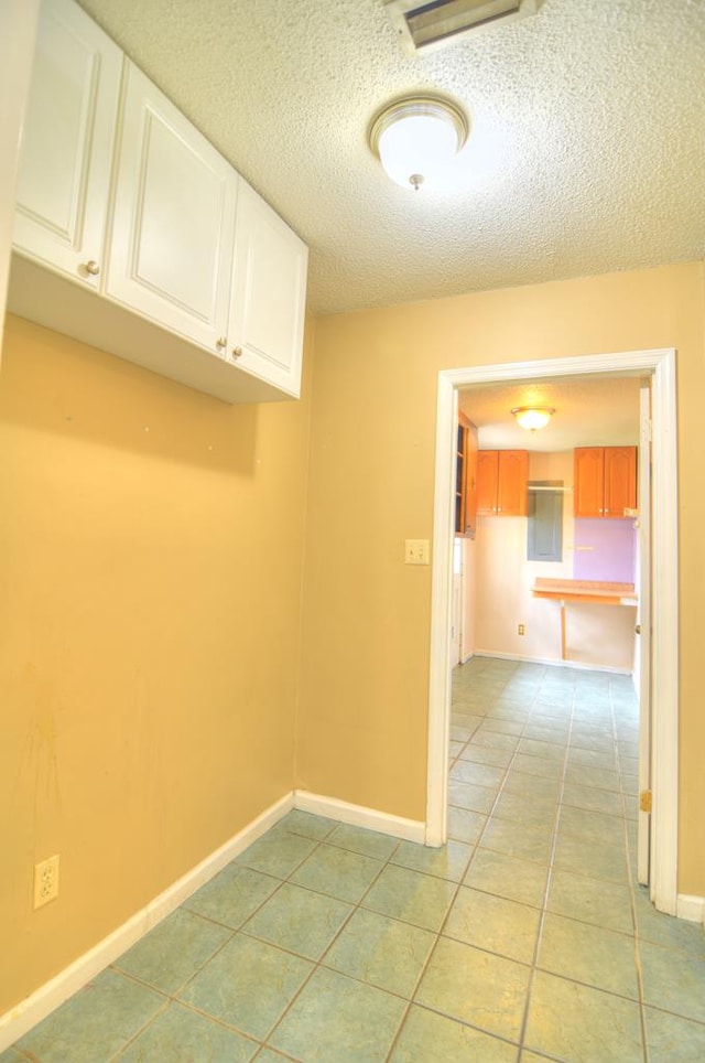 laundry room featuring light tile patterned flooring, cabinets, and a textured ceiling