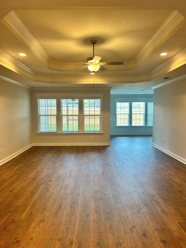 unfurnished room with ceiling fan, crown molding, dark wood-type flooring, and a tray ceiling