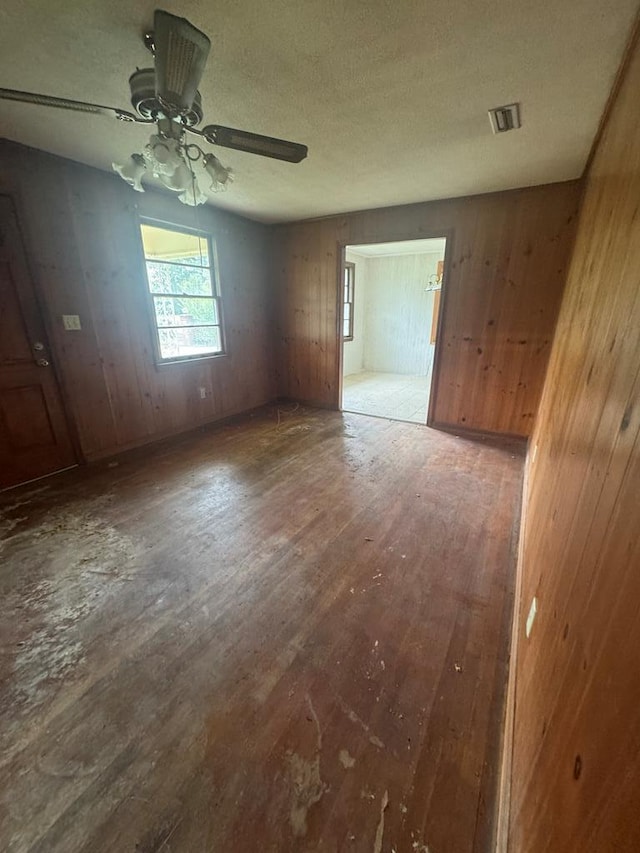 empty room with hardwood / wood-style floors, a textured ceiling, ceiling fan, and wood walls