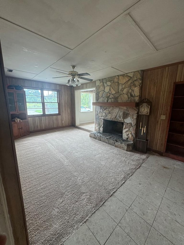 unfurnished living room with ceiling fan, light colored carpet, a fireplace, and wooden walls