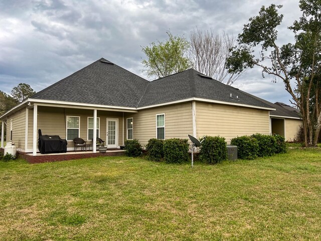 rear view of property with central air condition unit, a lawn, and roof with shingles