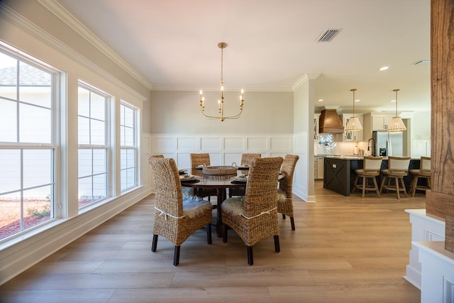 5039 Hatfield Cir, Hahira, GA 31632 - dining space featuring a chandelier, a wainscoted wall, crown molding, light wood-style flooring, and a decorative wall