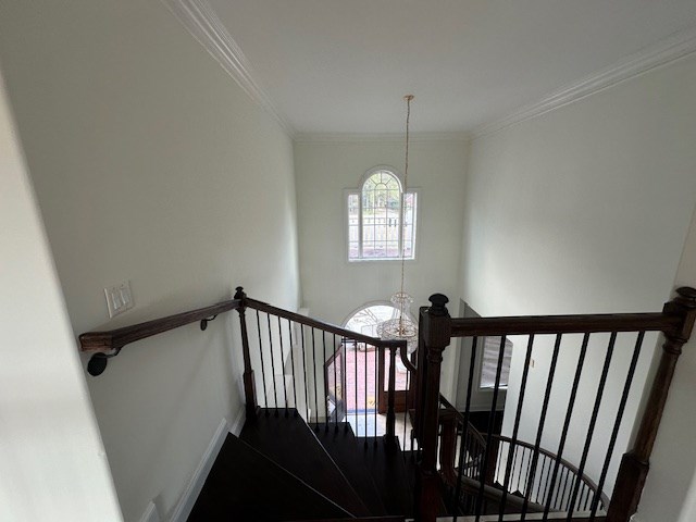 stairs featuring crown molding, a notable chandelier, and baseboards