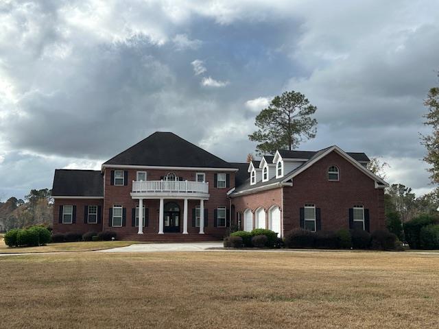 colonial home featuring a balcony and a front lawn