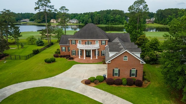 colonial house with a water view, a balcony, concrete driveway, and a front yard