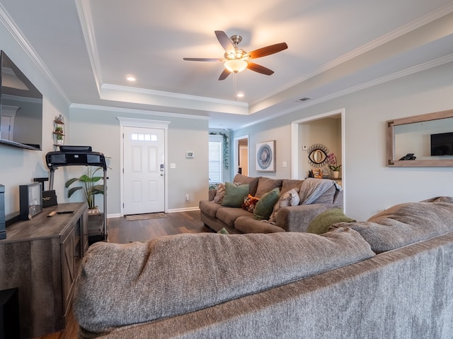 living room with dark wood-type flooring, ceiling fan, a tray ceiling, and crown molding