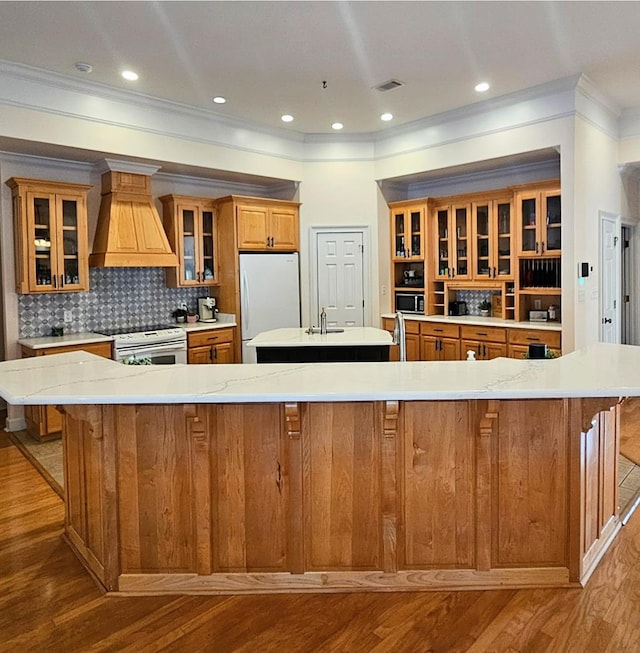 kitchen featuring white appliances, a breakfast bar area, custom range hood, and a large island with sink