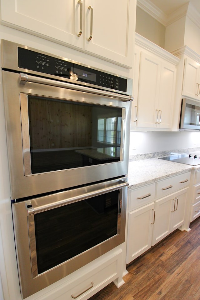 kitchen with appliances with stainless steel finishes, dark wood-style floors, ornamental molding, white cabinets, and light stone counters