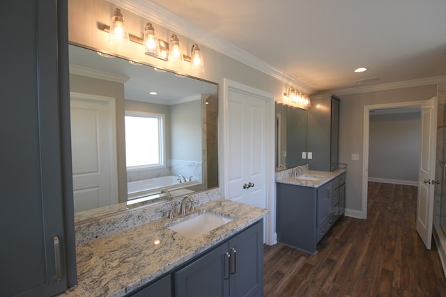 full bath featuring two vanities, wood finished floors, a bath, recessed lighting, and ornamental molding