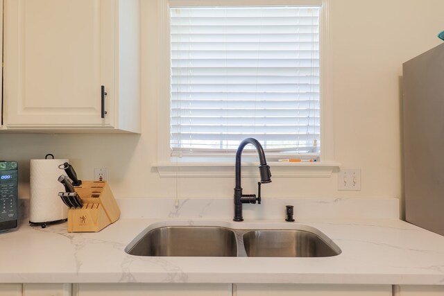 details featuring white cabinetry, light stone countertops, and sink