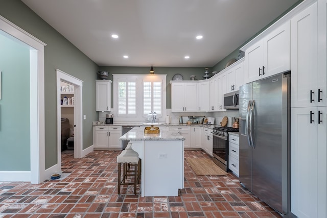 kitchen featuring light stone countertops, a kitchen breakfast bar, stainless steel appliances, a center island, and white cabinetry