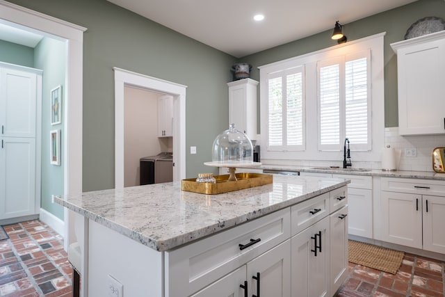 kitchen with white cabinetry, sink, a center island, light stone counters, and decorative backsplash