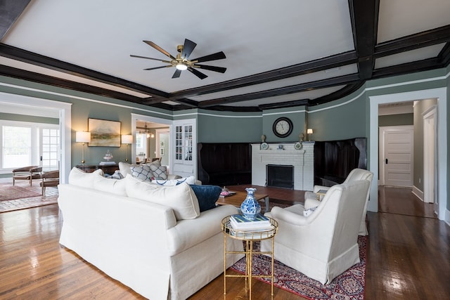 living room with ornamental molding, ceiling fan, wood-type flooring, beamed ceiling, and a fireplace