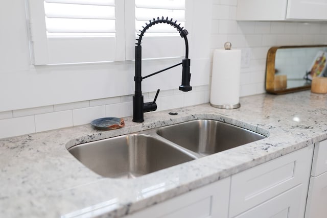 interior details with white cabinets, backsplash, light stone countertops, and sink