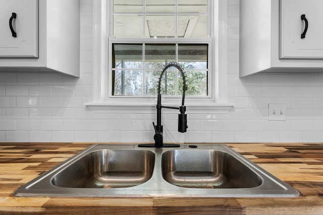 details with white cabinetry, a sink, wood counters, and decorative backsplash