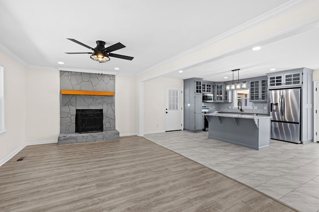 unfurnished living room featuring crown molding, visible vents, light wood-style flooring, a ceiling fan, and a stone fireplace