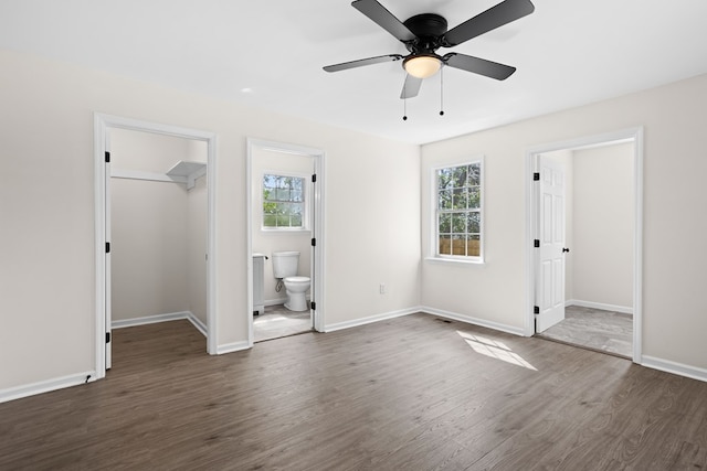 unfurnished bedroom featuring a closet, a spacious closet, ensuite bath, wood finished floors, and baseboards