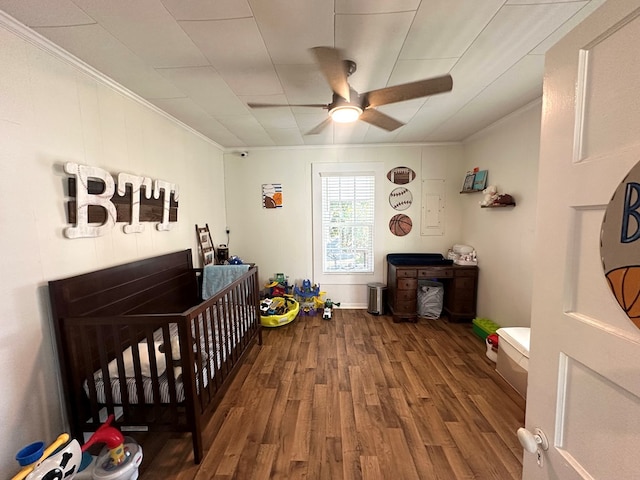 bedroom with crown molding, hardwood / wood-style flooring, a nursery area, and ceiling fan