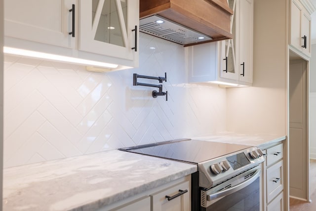 kitchen featuring electric stove, premium range hood, backsplash, light stone countertops, and white cabinets