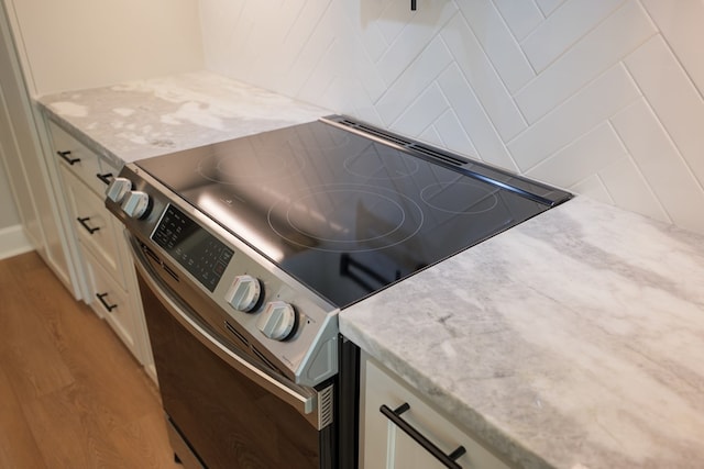 interior details with electric range, light stone countertops, white cabinets, and light wood-type flooring