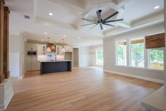 unfurnished living room featuring ceiling fan with notable chandelier, coffered ceiling, sink, and light wood-type flooring