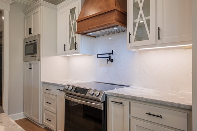 kitchen with light stone counters, custom range hood, stainless steel appliances, decorative backsplash, and white cabinets