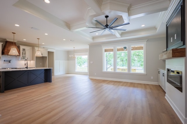 unfurnished living room featuring sink, ornamental molding, light hardwood / wood-style floors, a large fireplace, and ceiling fan with notable chandelier