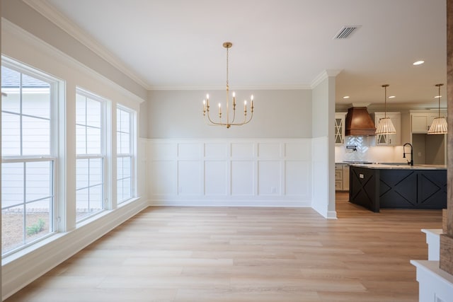 dining room with sink, ornamental molding, a chandelier, and light wood-type flooring