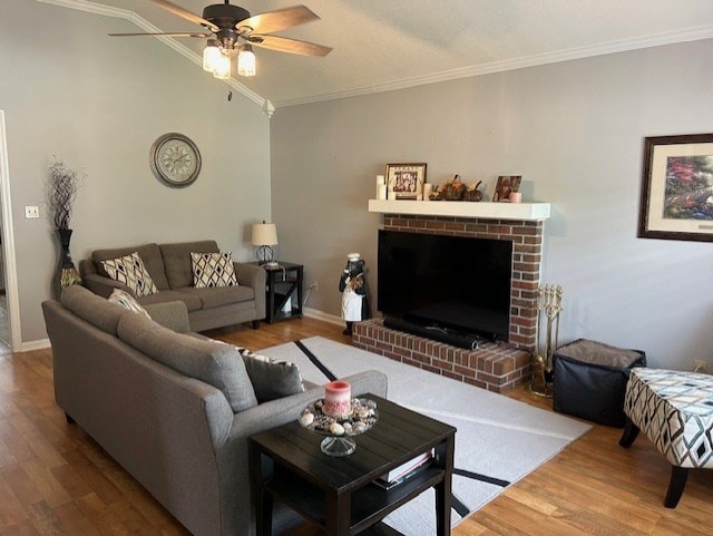 living room with lofted ceiling, a brick fireplace, wood finished floors, ceiling fan, and crown molding