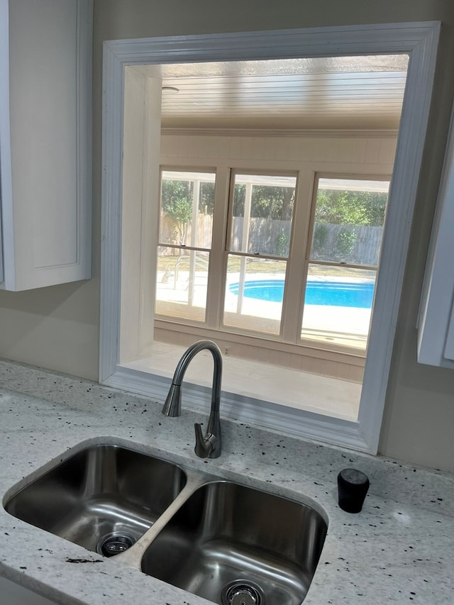 interior details with white cabinetry, light stone countertops, and sink