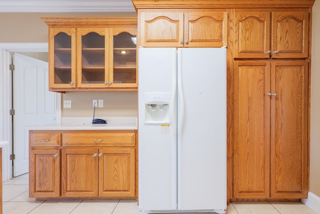 kitchen featuring white refrigerator with ice dispenser, brown cabinets, light tile patterned floors, light countertops, and glass insert cabinets