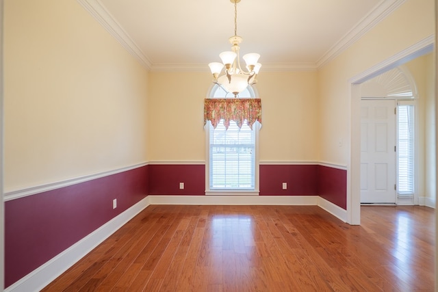 spare room featuring a chandelier, ornamental molding, wood finished floors, and baseboards